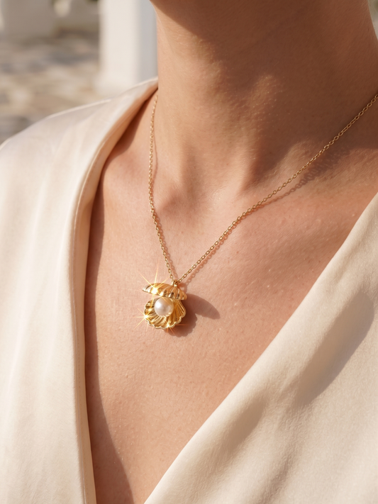 Gold necklace with a pendant featuring a pearl on a person wearing a light-colored top.