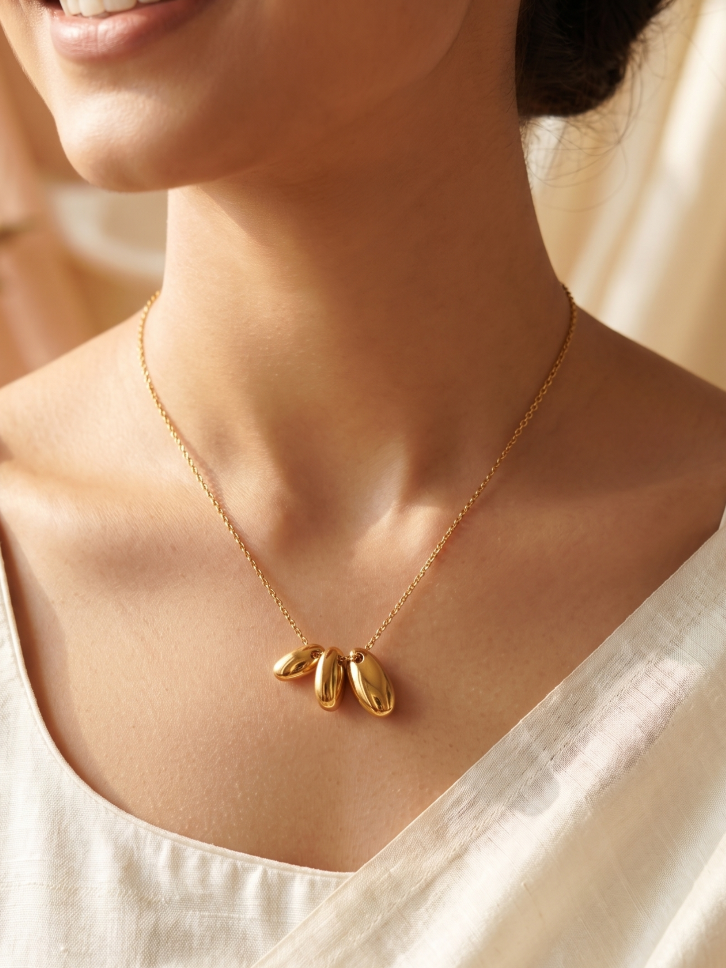 Gold necklace with a pendant worn by a person in a white top.