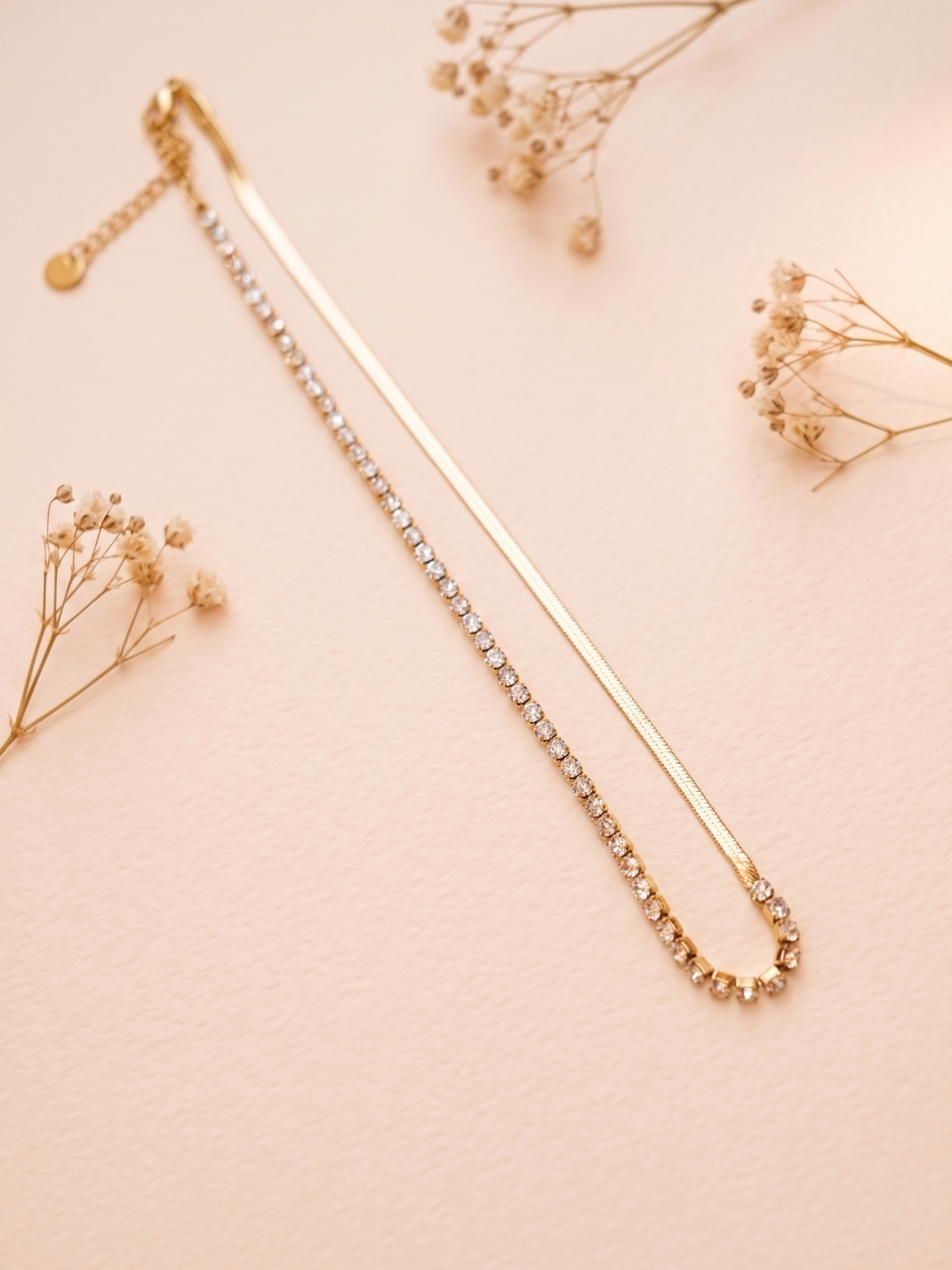 Gold necklace with small beads on a light pink background with dried flowers.