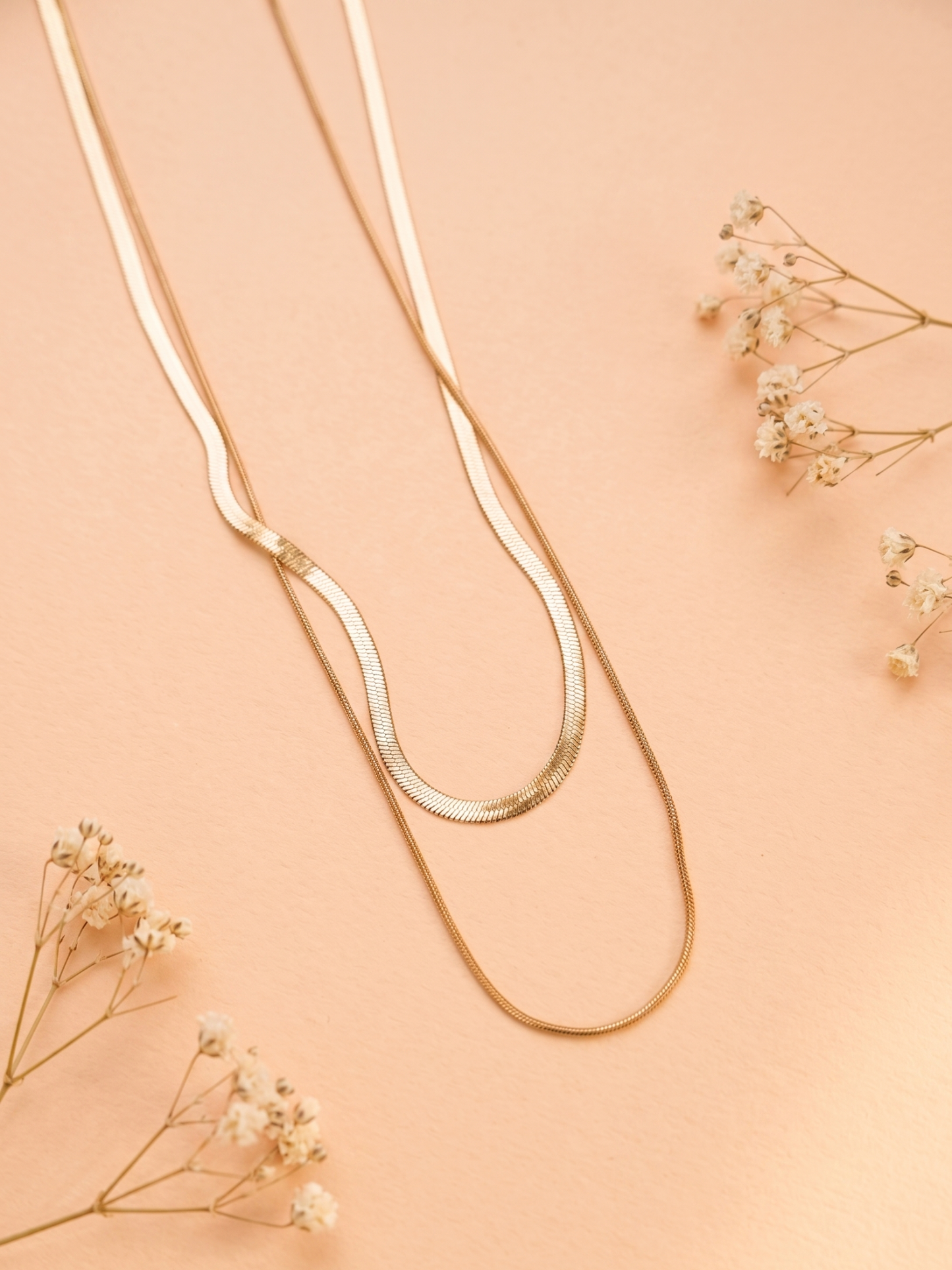Gold necklace on a peach background with dried flowers
