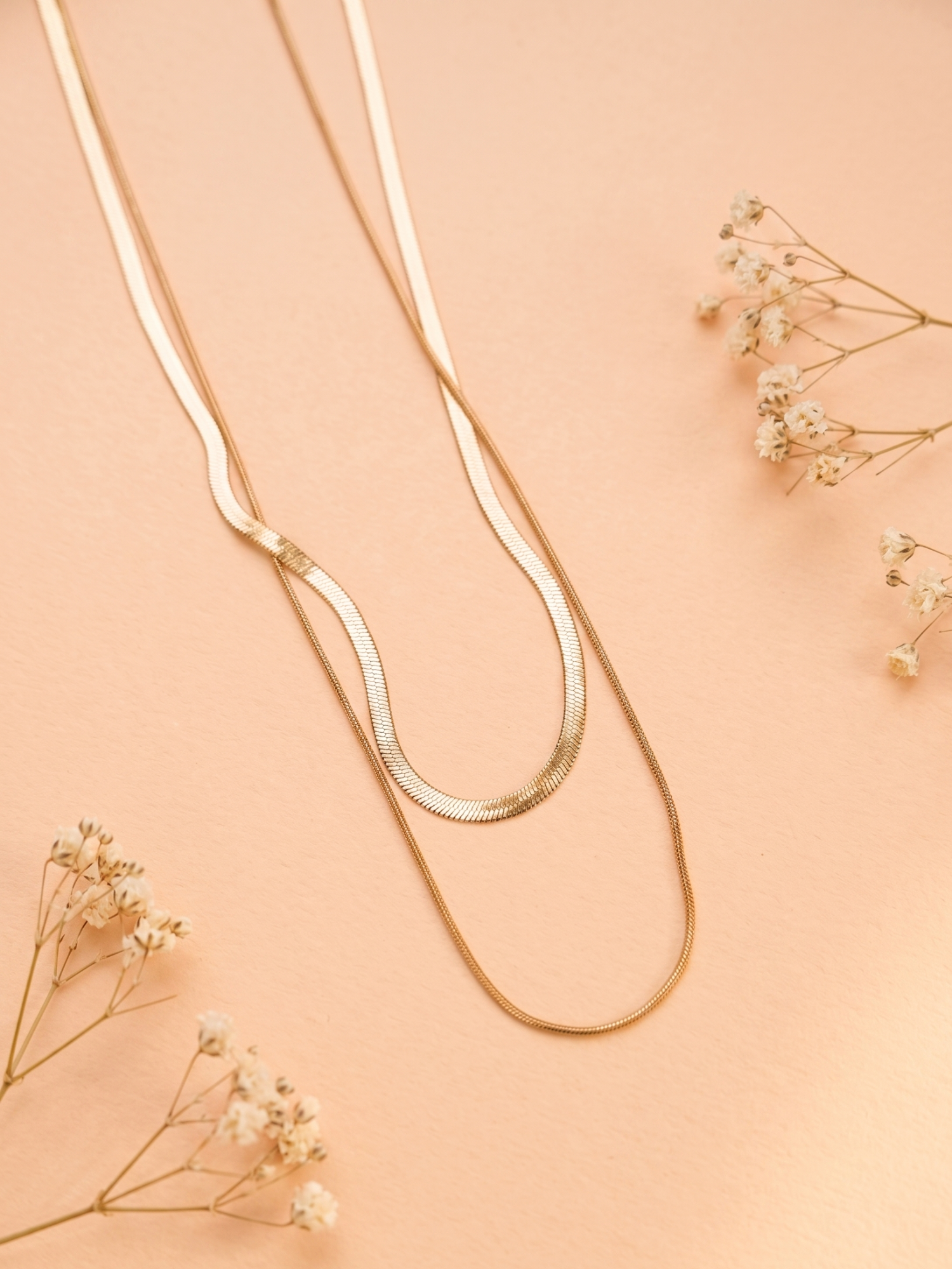 Gold necklace on a peach background with dried flowers