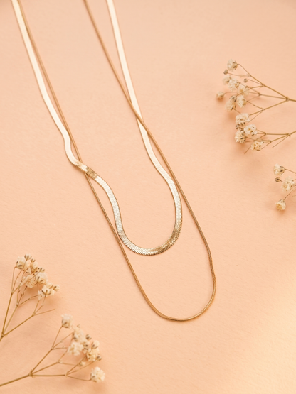 Gold necklace on a peach background with dried flowers