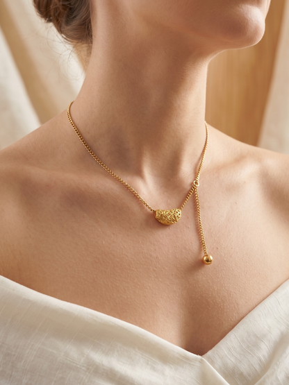 Gold necklace on a person wearing a white top with a neutral background