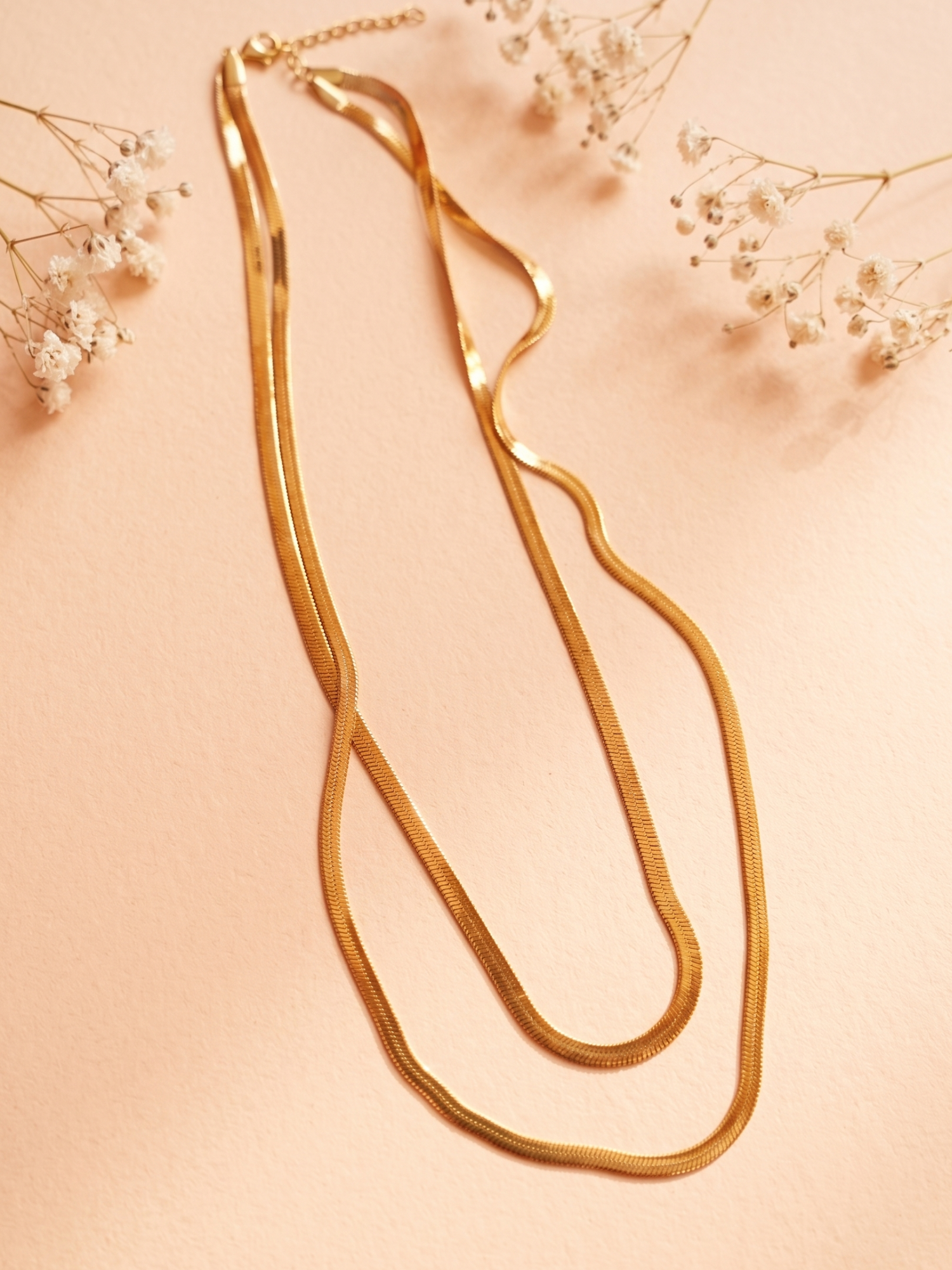 Gold necklace on a soft pink background with delicate flowers