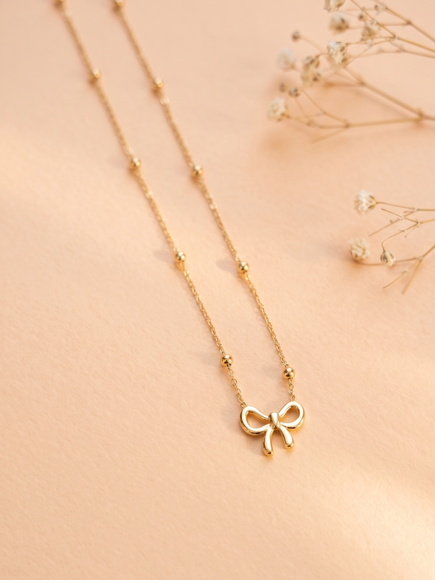 Gold necklace with a bow pendant on a beige background