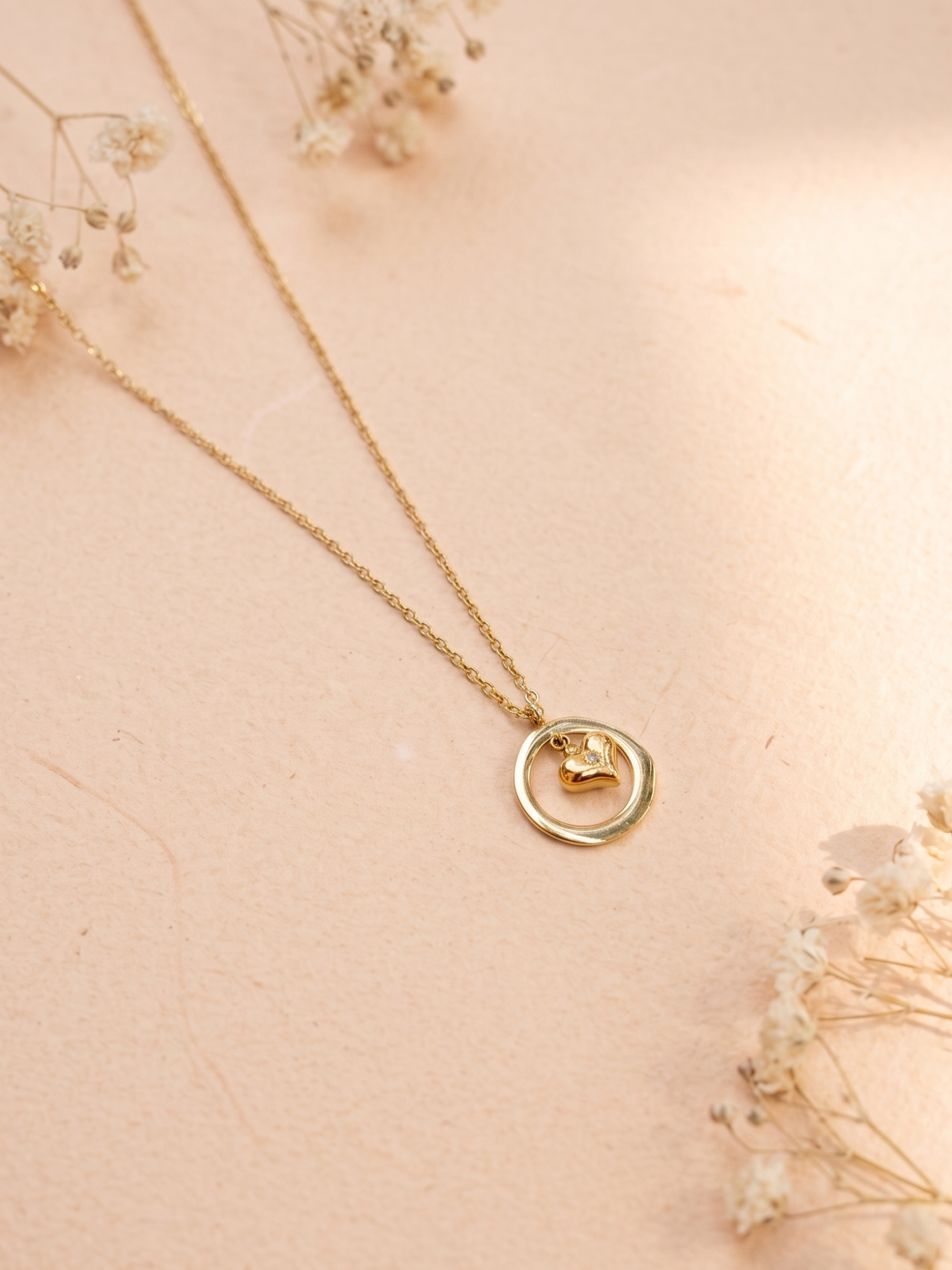 Gold necklace with a circular pendant on a soft pink background