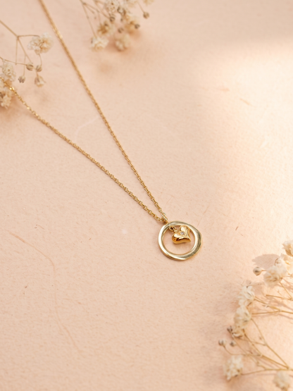 Gold necklace with a circular pendant on a soft pink background