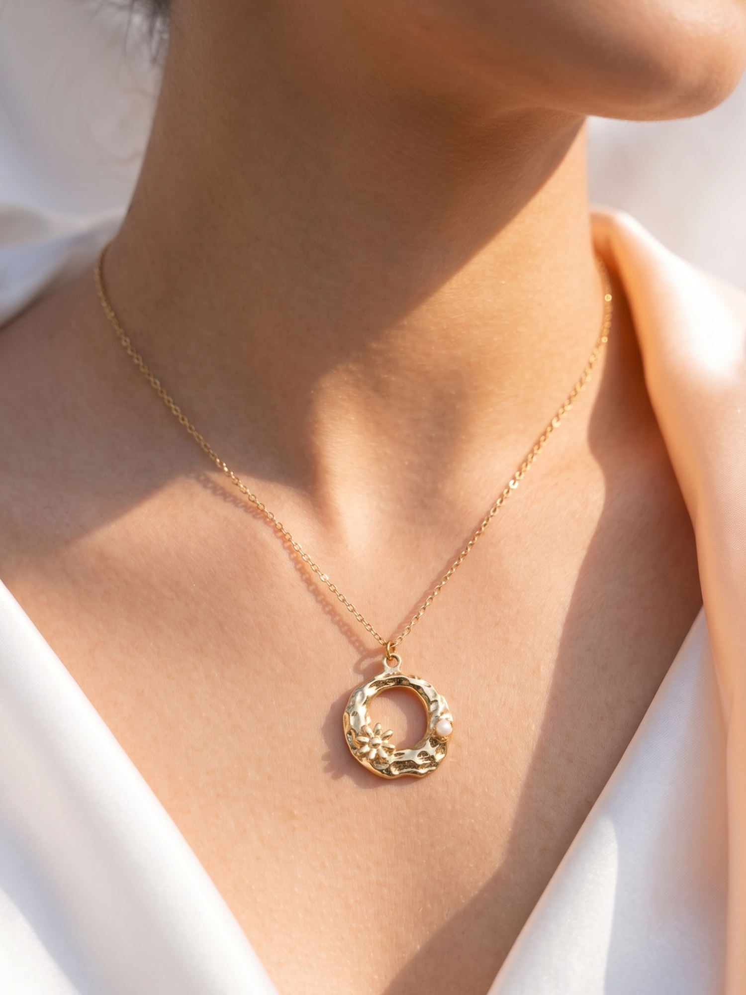 Gold necklace with a circular pendant on a person wearing a white top.