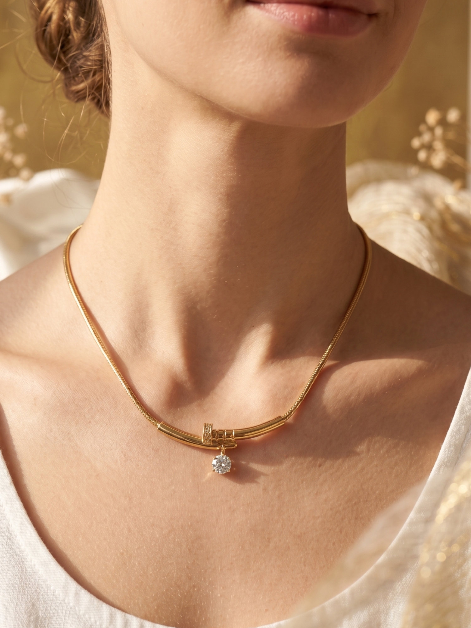 Gold necklace with a diamond pendant worn by a person against a blurred natural background