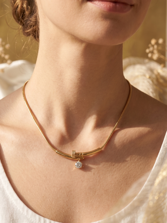 Gold necklace with a diamond pendant worn by a person against a blurred natural background