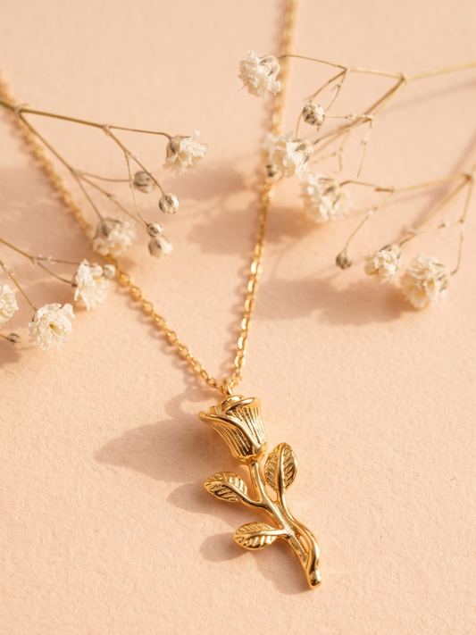 Gold necklace with a floral pendant on a soft pink background