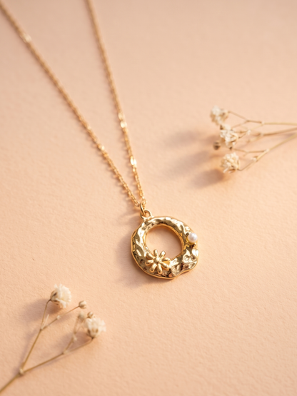 Gold necklace with a floral pendant on a soft beige background