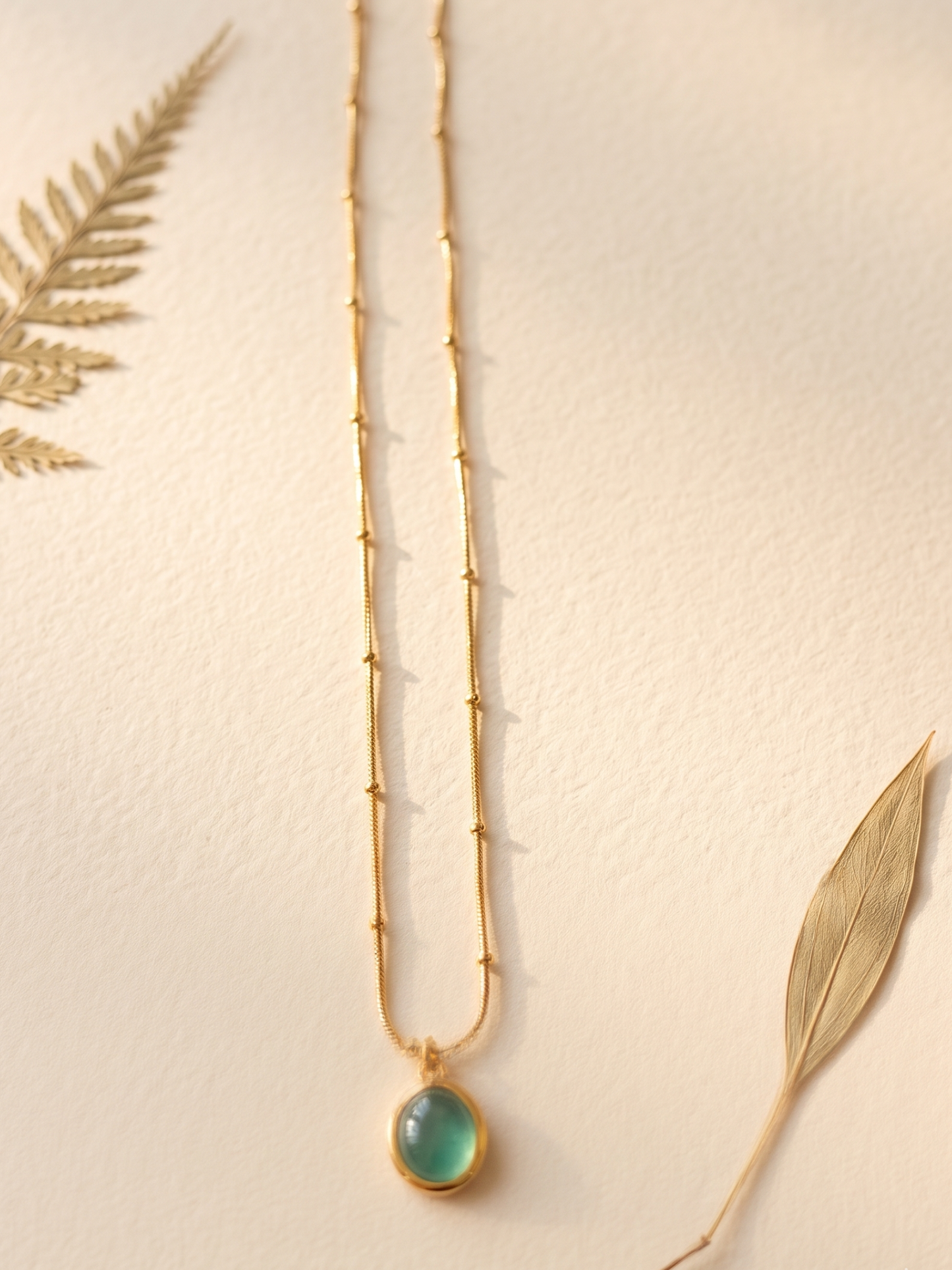 Gold necklace with a green pendant leaves.