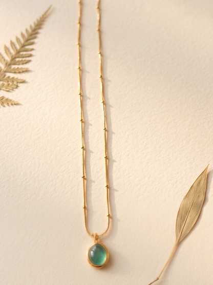 Gold necklace with a green pendant leaves.