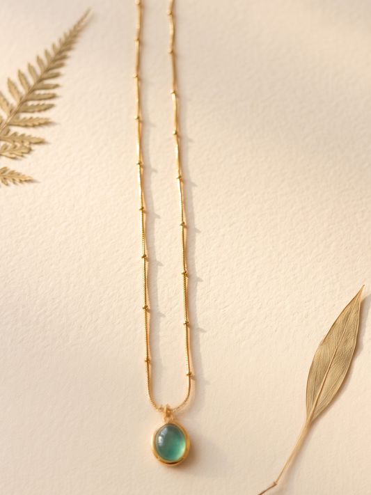 Gold necklace with a green pendant leaves.