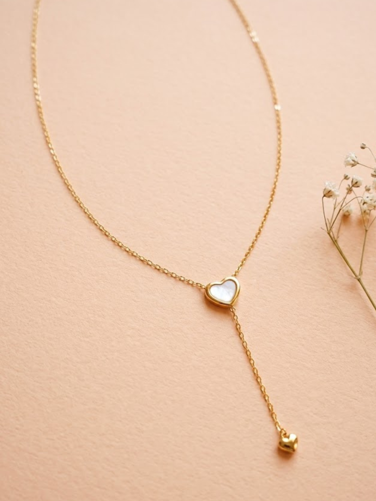 Gold necklace with a heart-shaped pendant on a beige background
