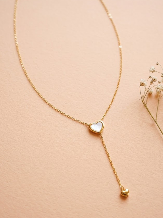 Gold necklace with a heart-shaped pendant on a beige background