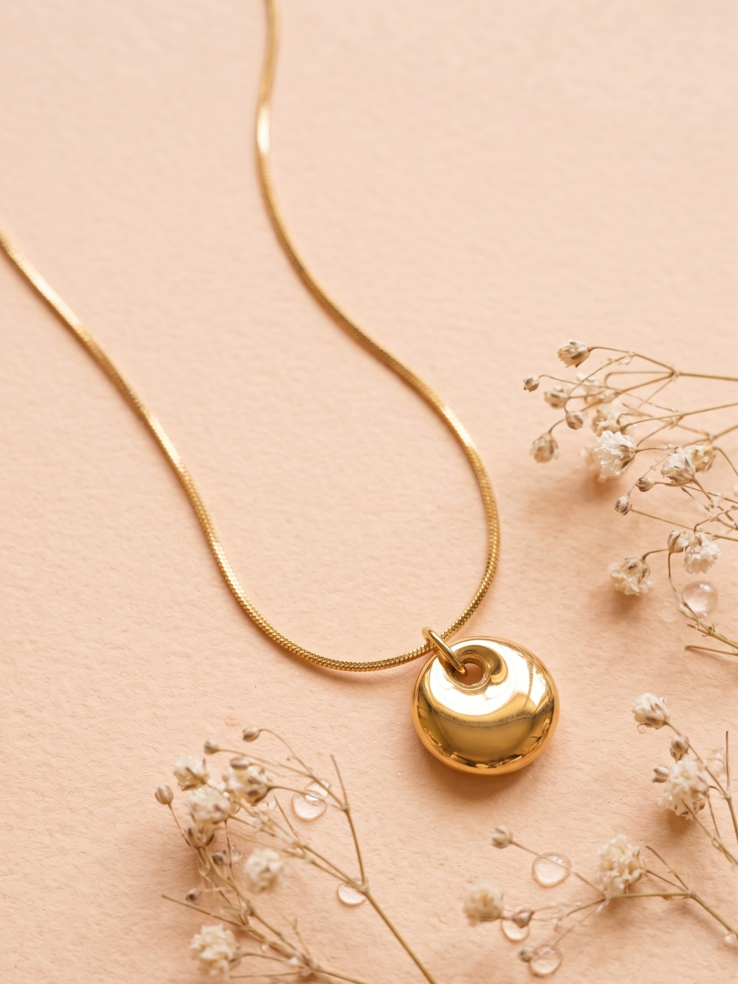 Gold necklace with a heart-shaped pendant on a beige background with small flowers.