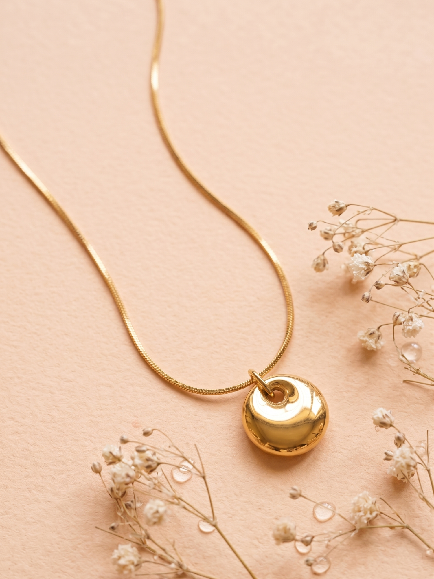Gold necklace with a heart-shaped pendant on a beige background with small flowers.
