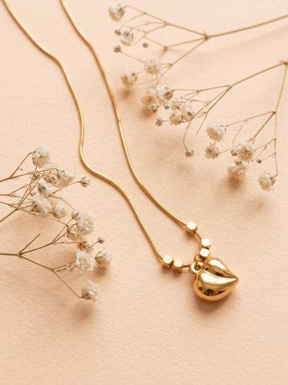 Gold necklace with a heart pendant on a beige background with dried flowers.