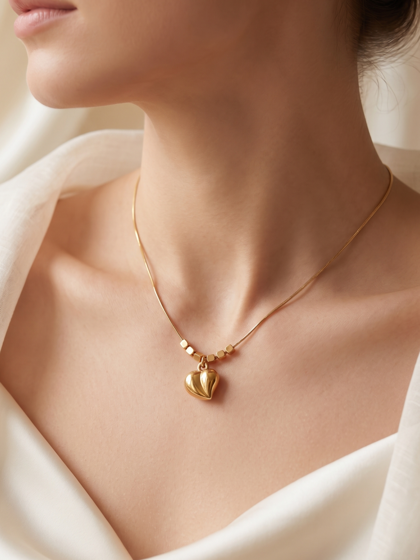 Gold necklace with a heart pendant on a person wearing a white garment