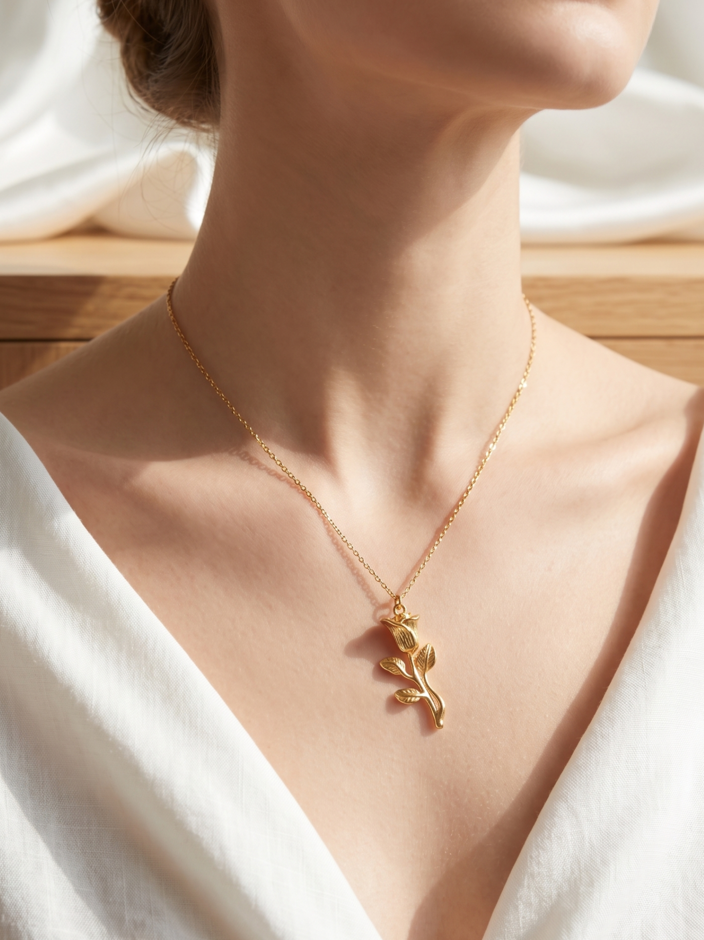 Gold necklace with a leaf pendant on a person wearing a white top.