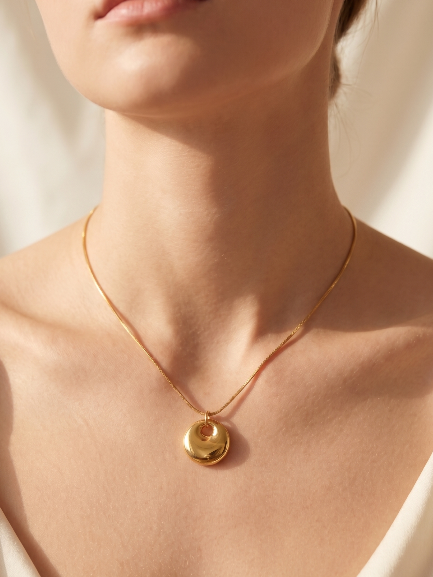 Gold necklace with a pendant on a person wearing a white top against a neutral background