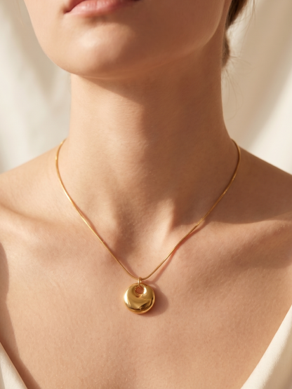 Gold necklace with a pendant on a person wearing a white top against a neutral background