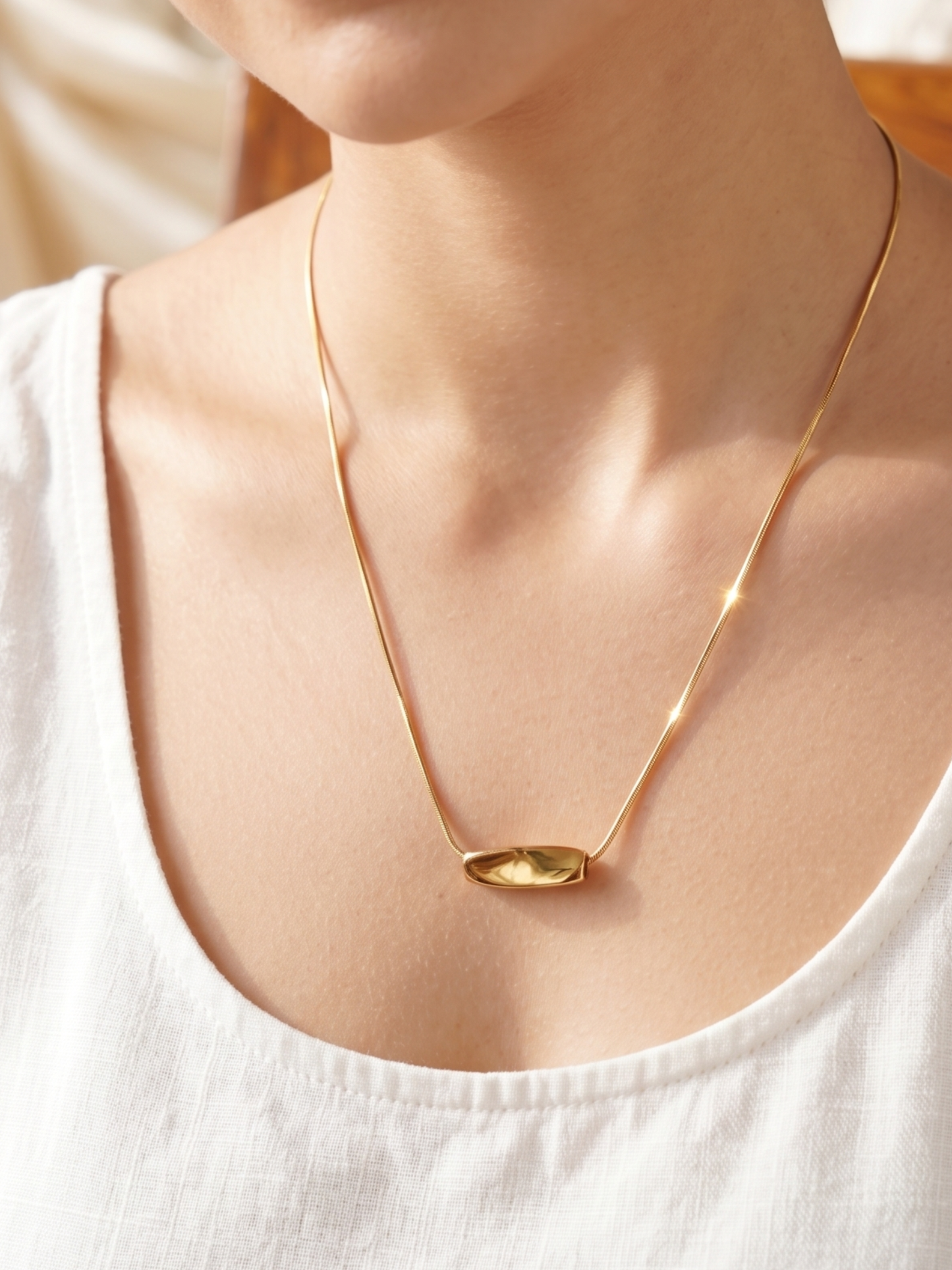 Gold necklace with a pendant on a person wearing a white top.