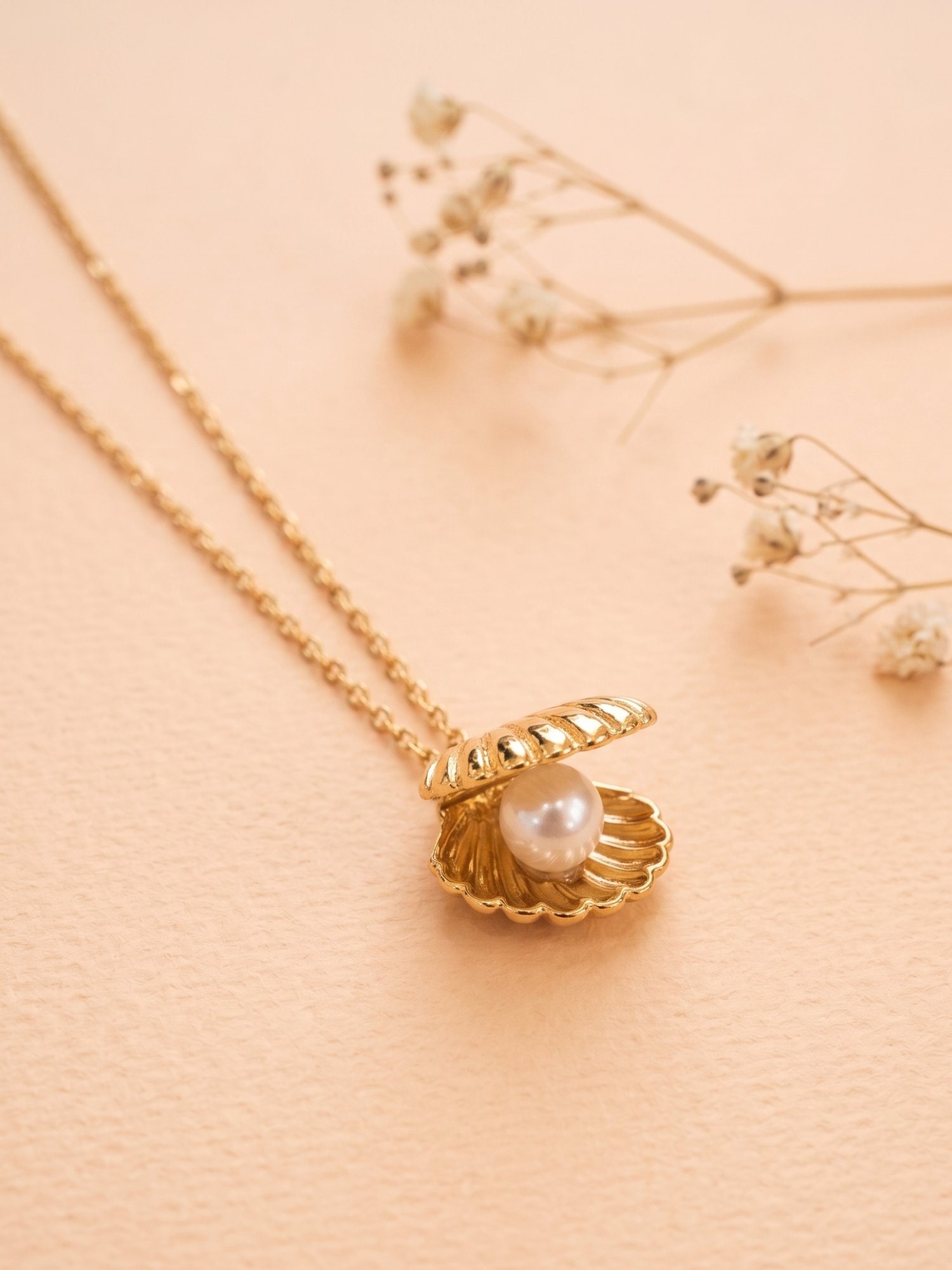 Gold necklace with a shell pendant featuring a pearl on a soft pink background