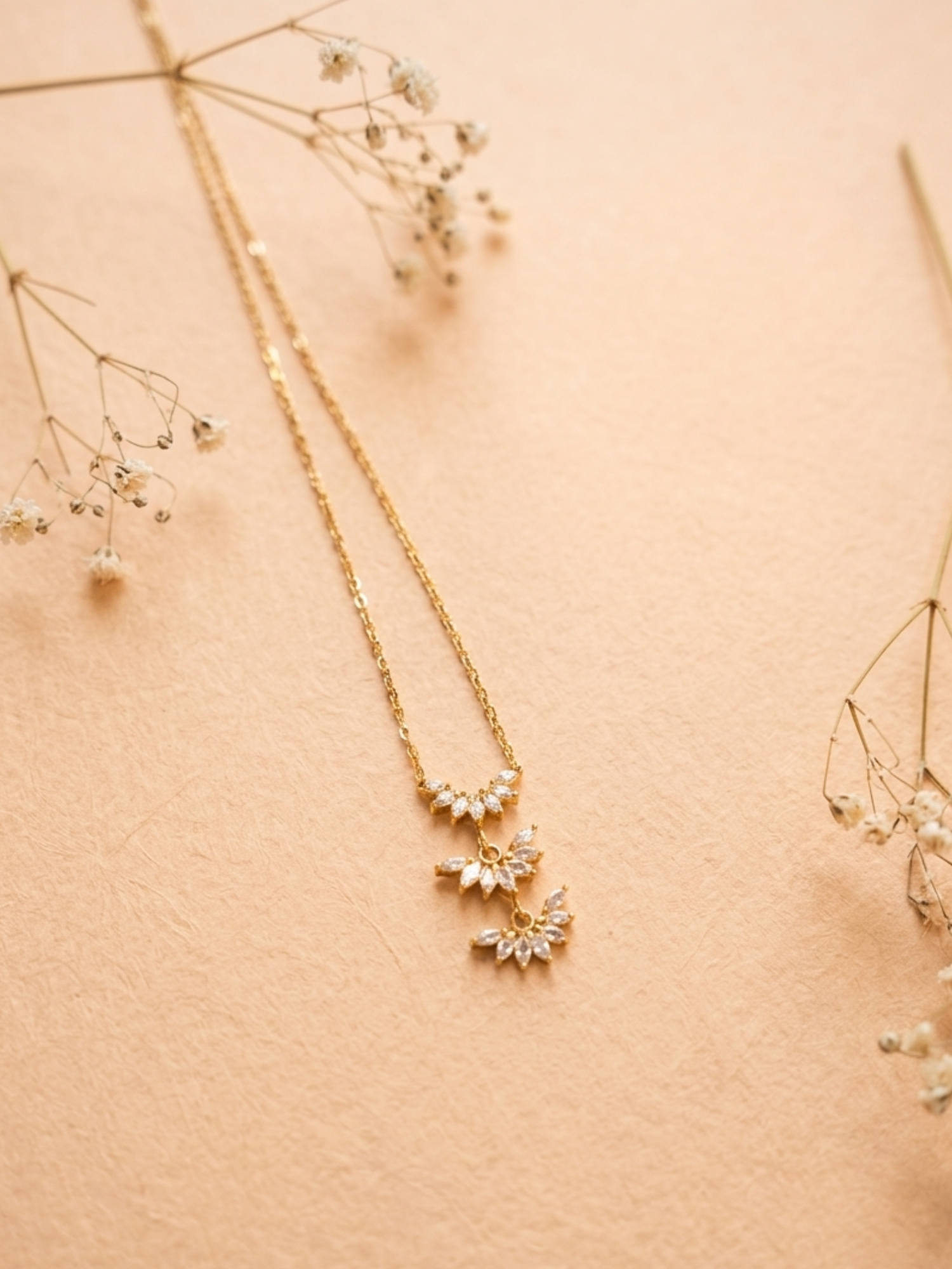 Gold necklace with floral pendant on a beige background