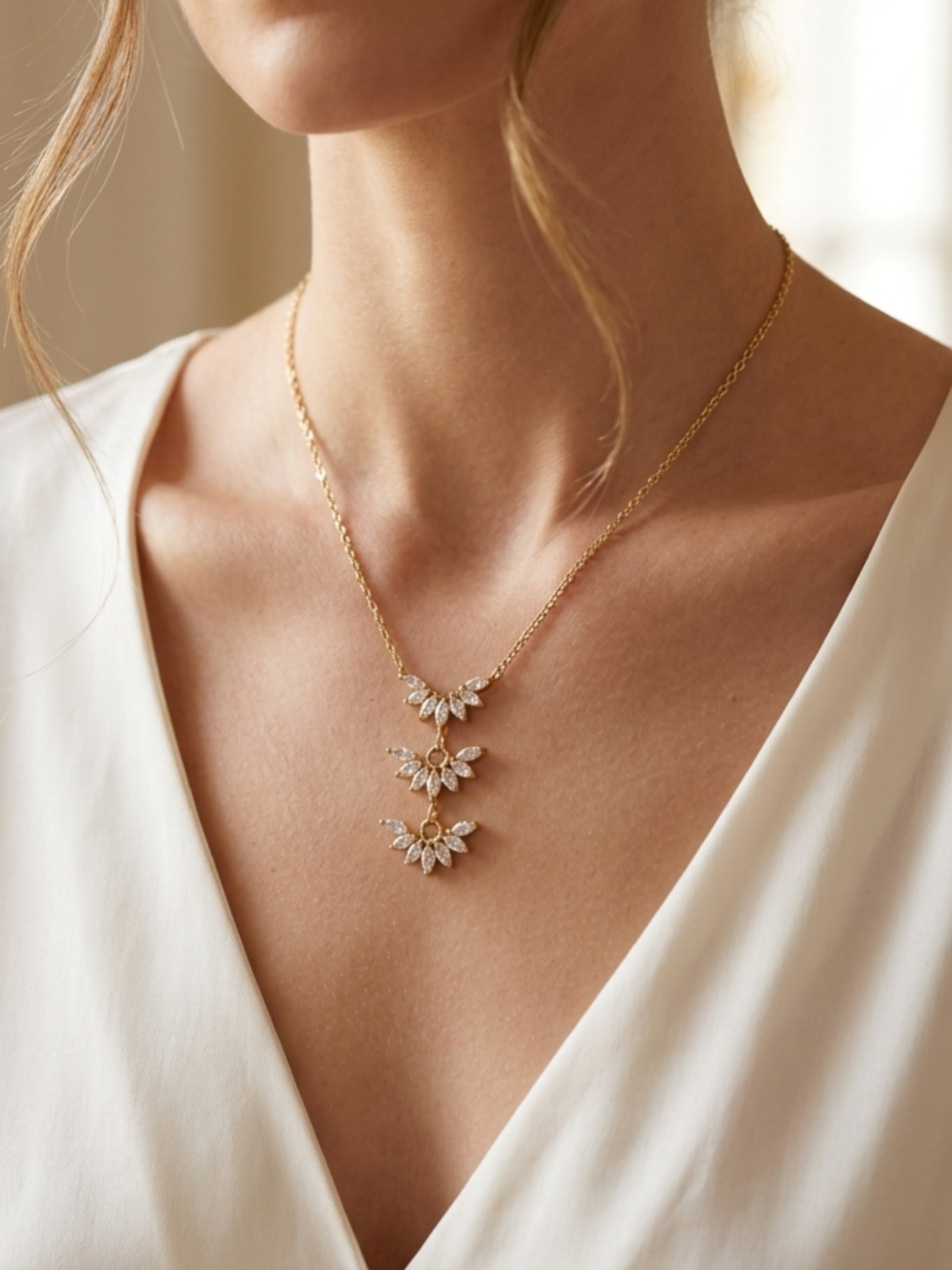 Gold necklace with floral pendants on a person wearing a white top.