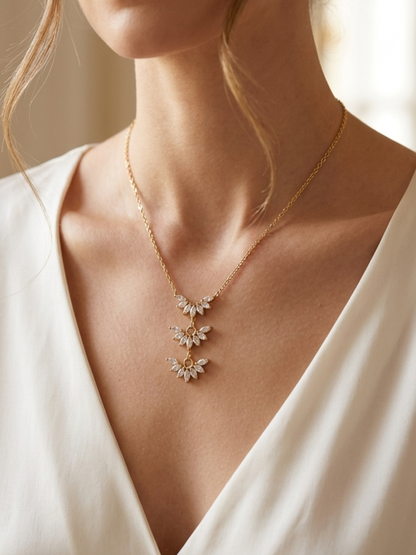 Gold necklace with floral pendants on a person wearing a white top.
