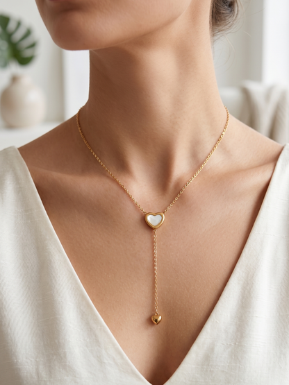 Gold necklace with heart-shaped pendant worn by a person in a white top.