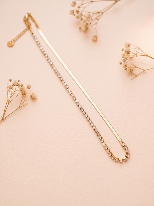 Gold necklace with small beads on a light pink background with dried flowers.
