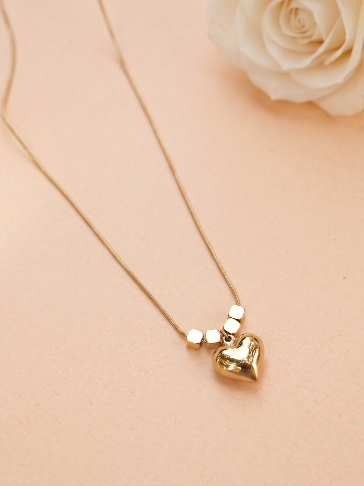 Gold heart-shaped pendant necklace on a beige background