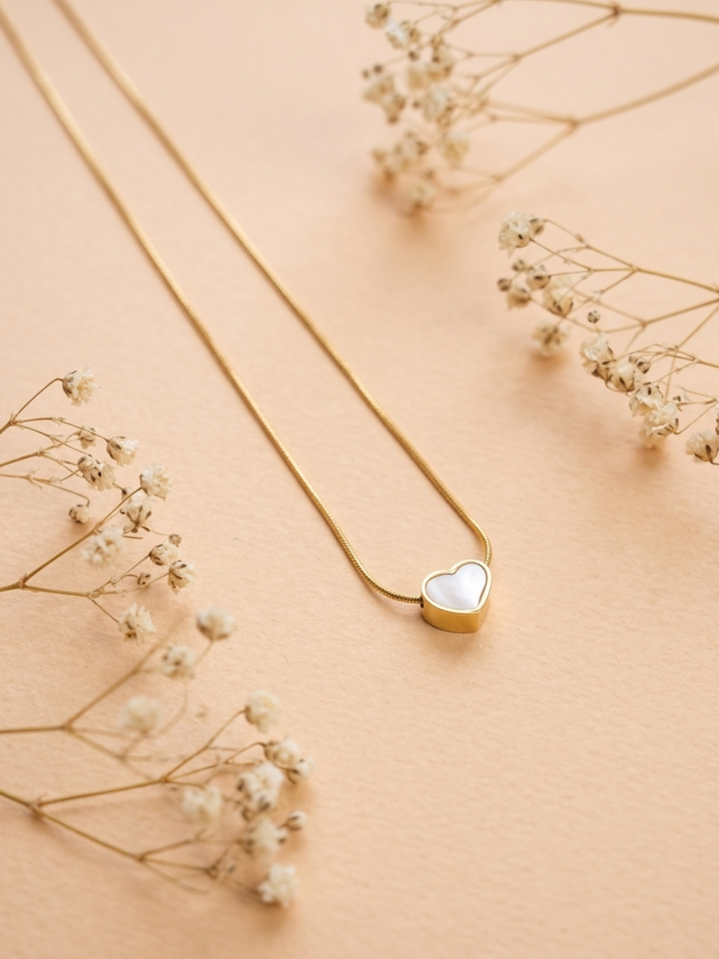 Gold necklace with a heart-shaped pendant on a beige background with delicate flowers.