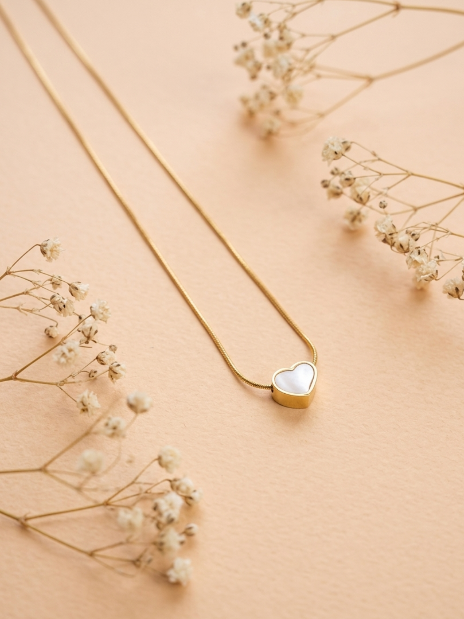 Gold necklace with a heart-shaped pendant on a beige background with delicate flowers.