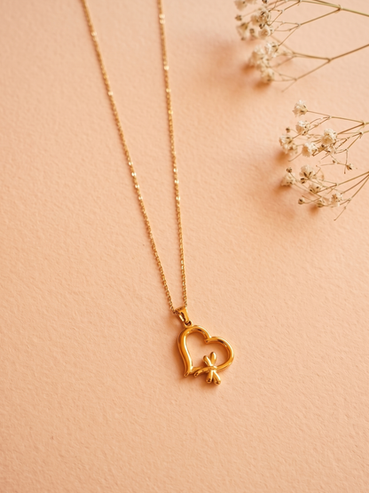 Gold necklace with a heart-shaped pendant on a soft pink background